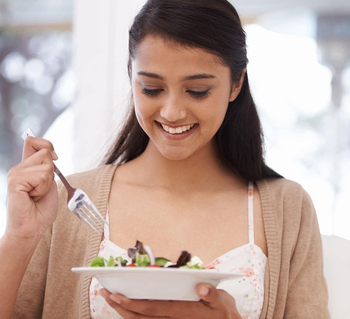 A woman eating a salad with a fork.